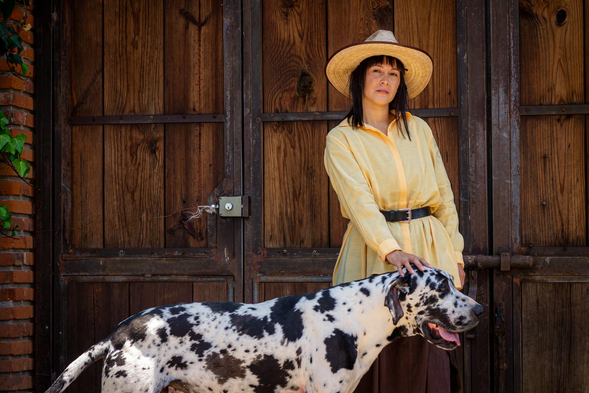 Woman in Yellow Long Sleeve Shirt and Brown Straw Hat Standing Beside Dalmatian Dog