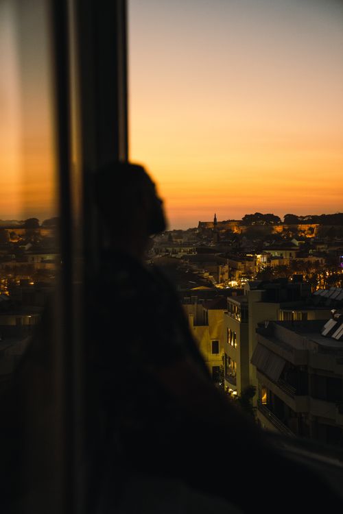 Free Silhouette of a person gazing at a vibrant sunset over a cityscape, creating a serene urban atmosphere. Stock Photo