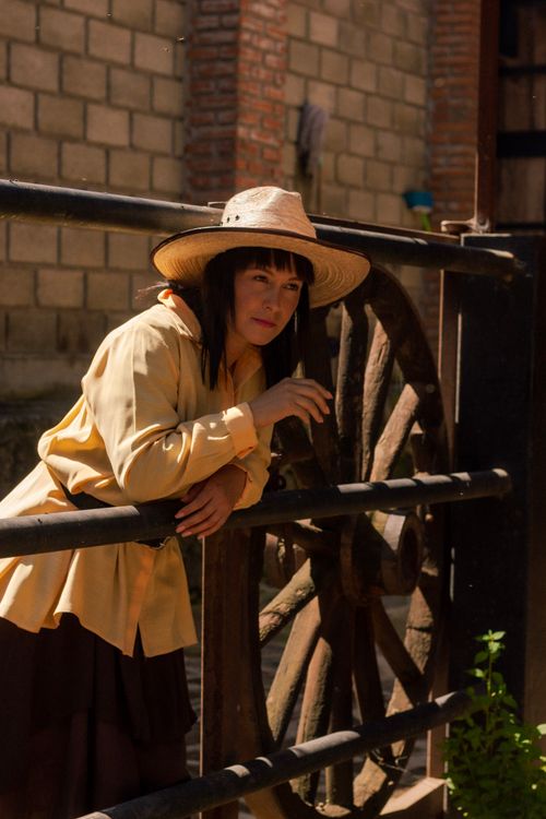 Free Woman in straw hat and yellow sleeves leaning on farm fence with rustic wooden wheel Stock Photo