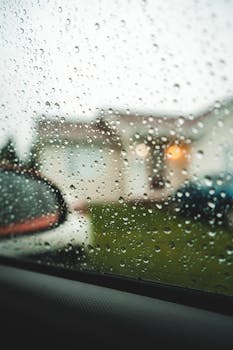 Close-up of raindrops on a car window with a blurred residential street background