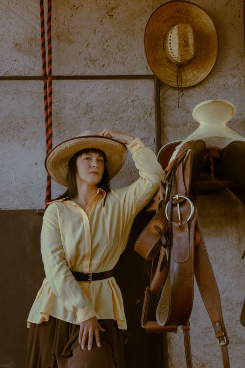 Free A woman wearing a cowboy hat poses by a saddle, showcasing Mexican style. Stock Photo