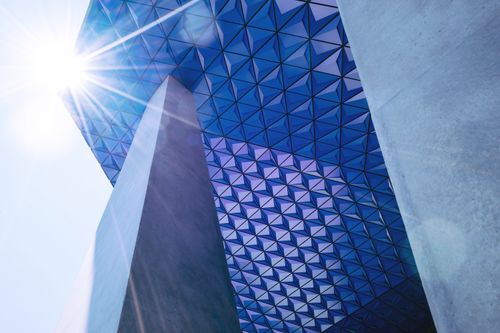 Free A modern skyscraper with a geometric facade and sun glare creating a dramatic effect. Stock Photo
