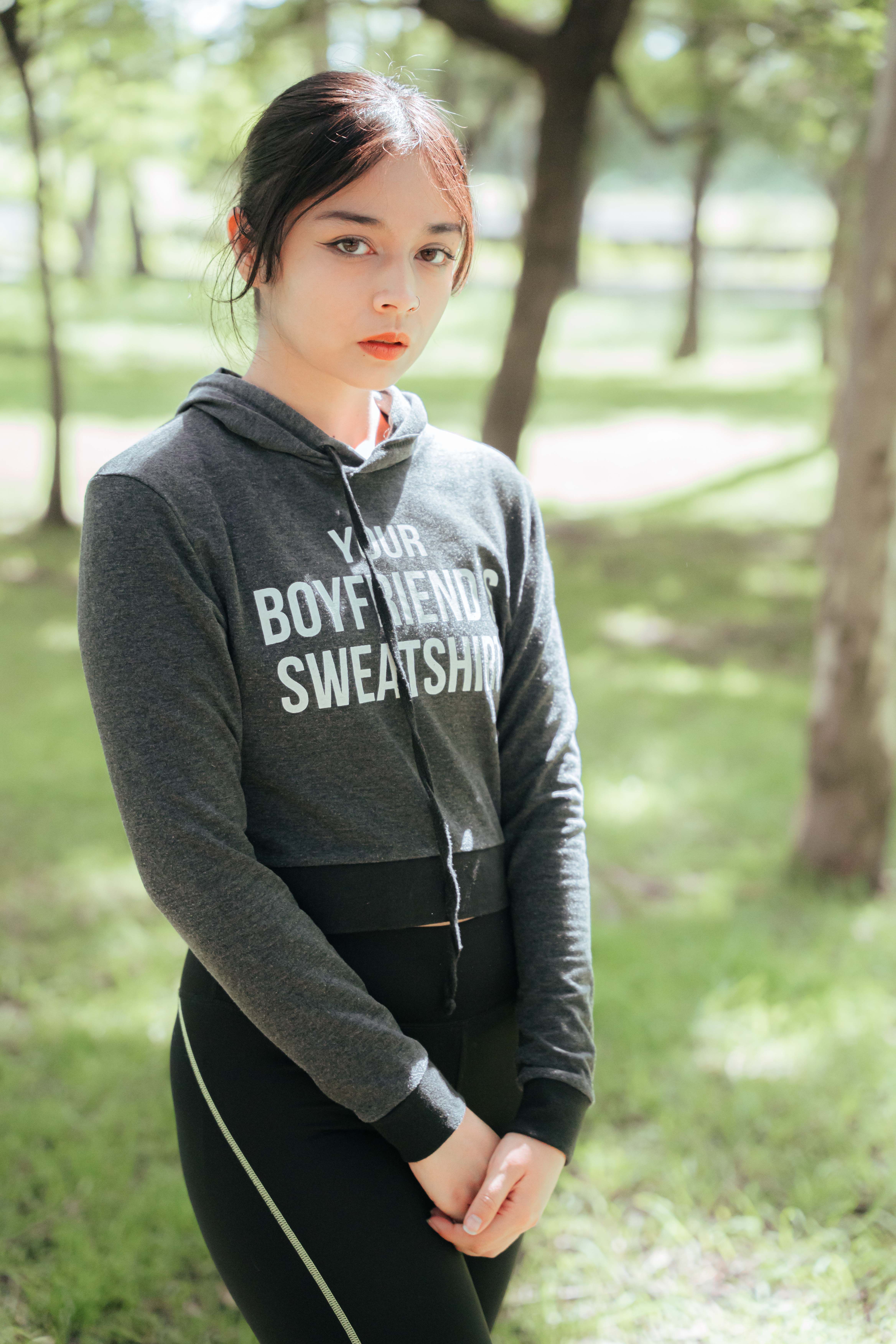 Woman wearing a hoodie in a sunny park setting, facing the camera.