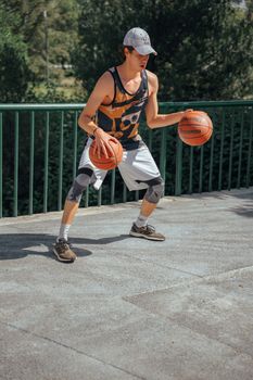 Young man practicing basketball dribbling with two balls outdoors in sportswear.