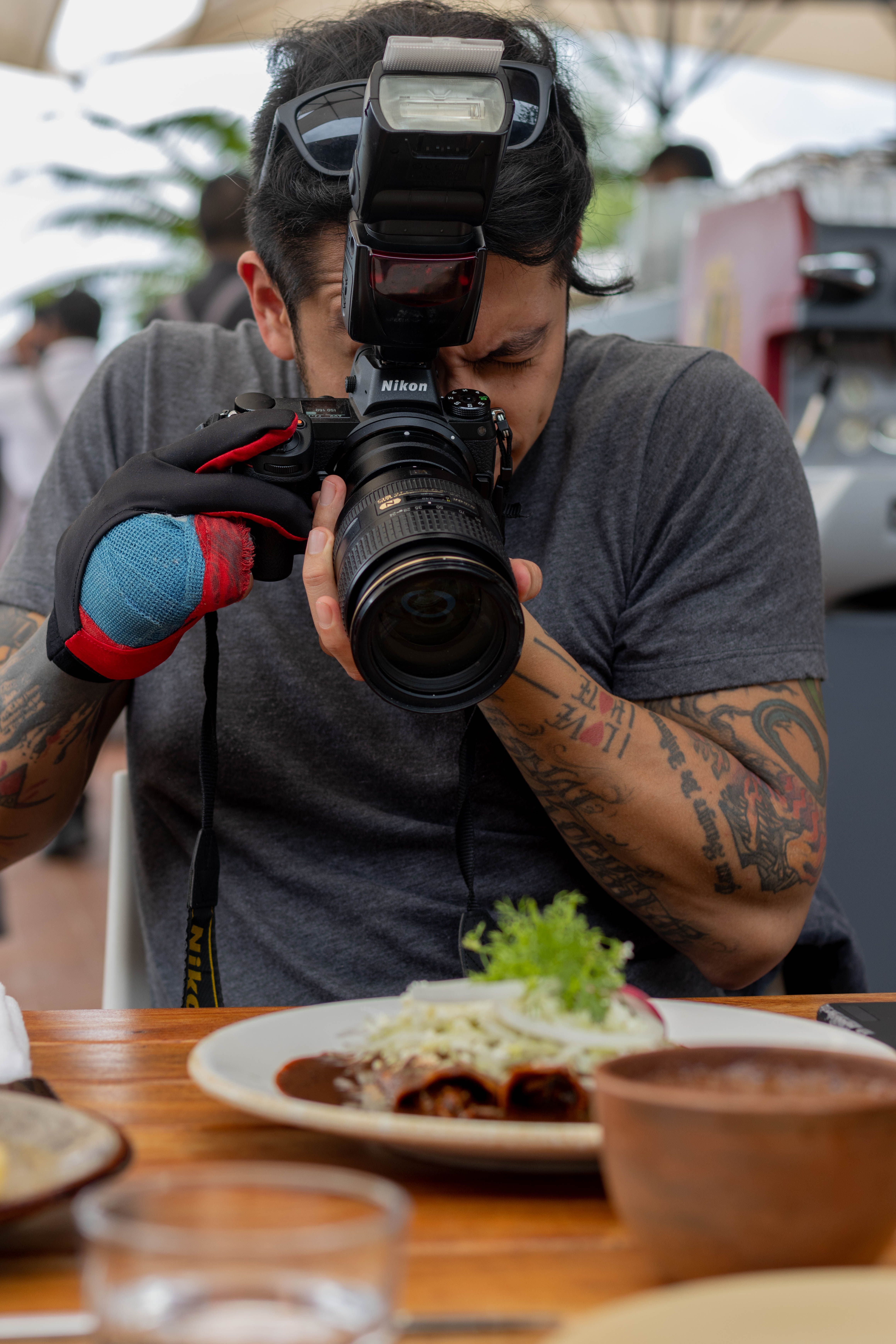 A tattooed photographer focuses on capturing a gourmet dish at a restaurant.