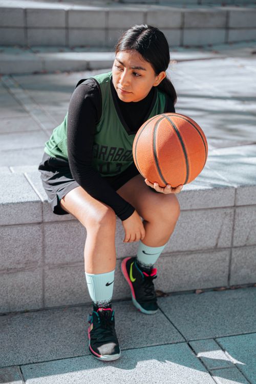 Free A young woman athlete in sportswear sitting outdoors with a basketball, full of focus. Stock Photo