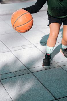 A young player dribbling a basketball on an outdoor court in sunlight.