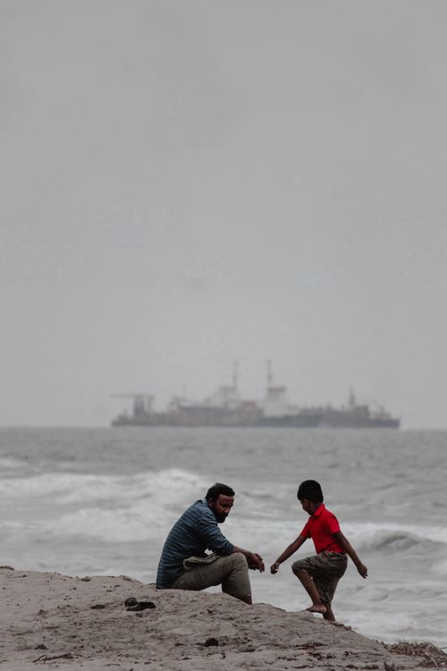 Free Father and son bonding at Kochi beach with a ship in the backdrop on an overcast day. Stock Photo