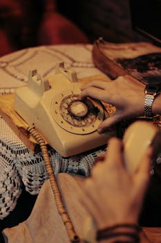 Hands dialing a vintage rotary phone on a lace-covered table, evoking nostalgia.