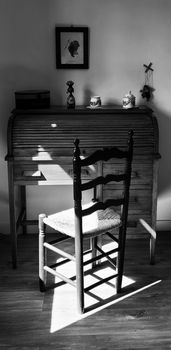 Black and white photo of a wooden chair and desk in a sunlit room in Barcelona, Spain.