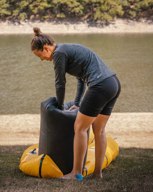 Young Woman Packing an Inflatable Item while Standing near a Body of Water and Smiling 