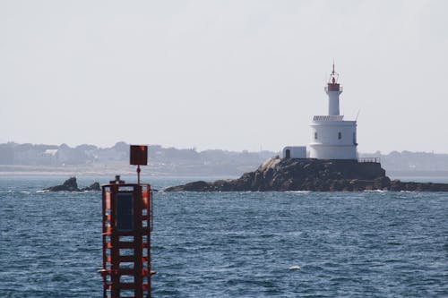 White and Red Lighthouse on Rock Formation Near Sea