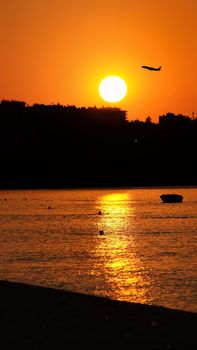 A breathtaking sunset over the ocean with a silhouette of a plane in flight, capturing tranquility and adventure.