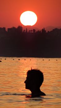 A picturesque scene of a man swimming in a tranquil lake at sunset with a vibrant sky.