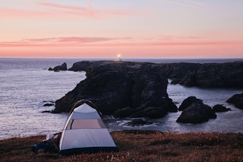 White Dome Tent on Black Rock Formation Near Body of Water during Sunset