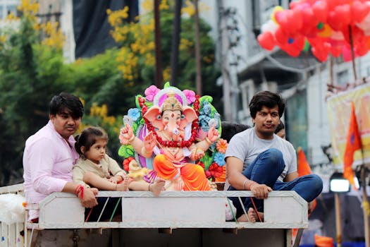 Colorful Ganesh idol with family during festive street procession.