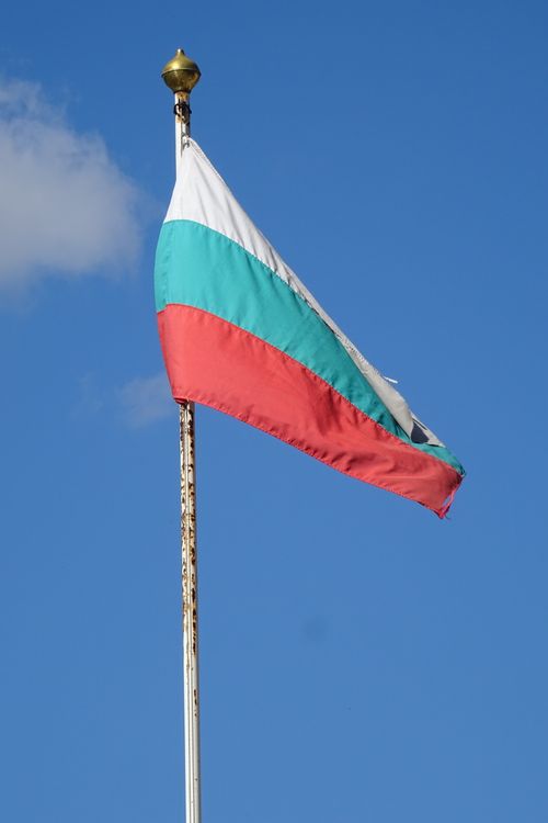 Free High-definition image of the Bulgarian national flag on a flagpole, waving in a vibrant blue sky. Stock Photo