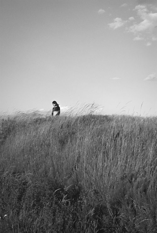 Free A solitary woman strolls through a vast grass field, captured in monochrome, evoking a sense of wanderlust and adventure. Stock Photo