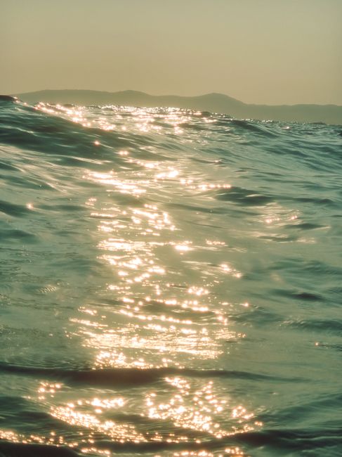 Beautiful sunlit ocean waves with distant hills at sunrise, serene seascape view.