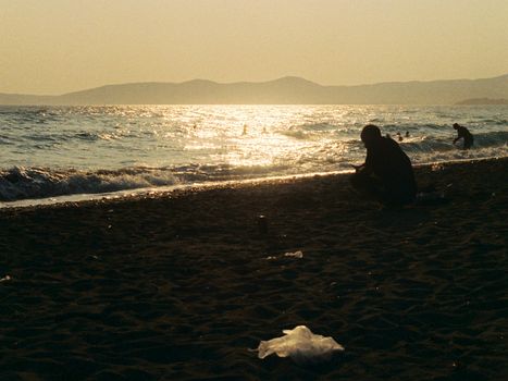 Silhouettes of people enjoying a serene beach at sunset with shimmering sea waves.