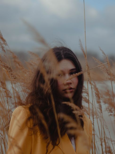 Artistic portrait of a woman in tall grass with a moody, windy vibe.