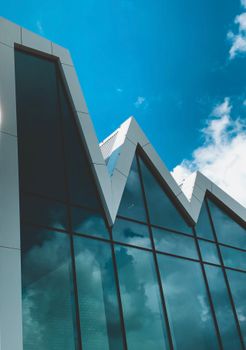 Futuristic glass building with angular design in Halfweg, Netherlands, against a blue sky.