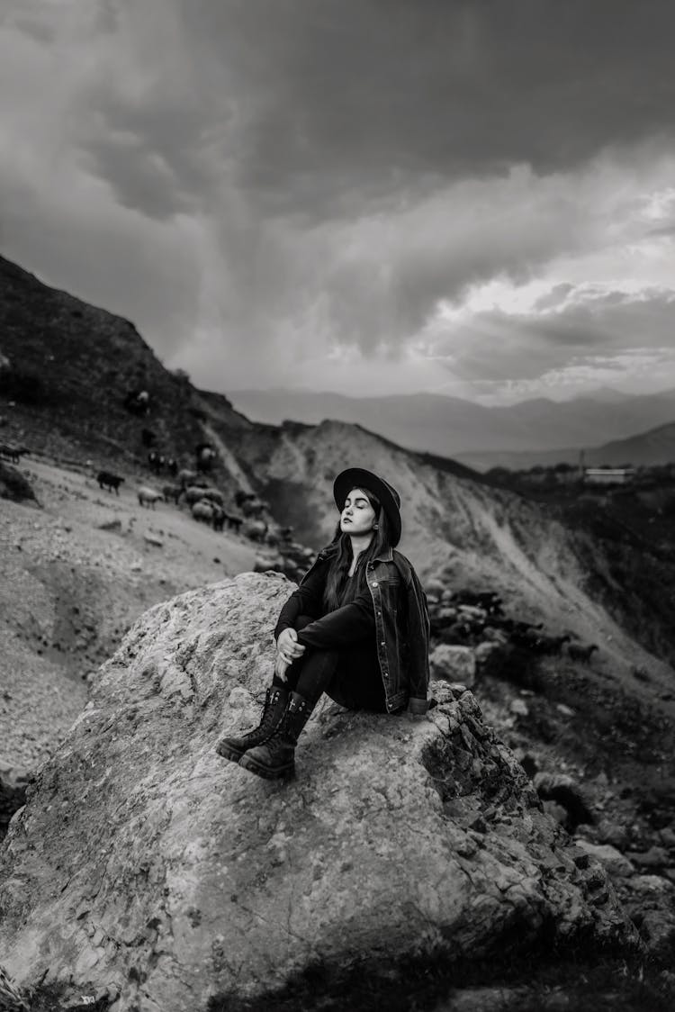 Woman Sitting On Top Of A Rocky Mountain