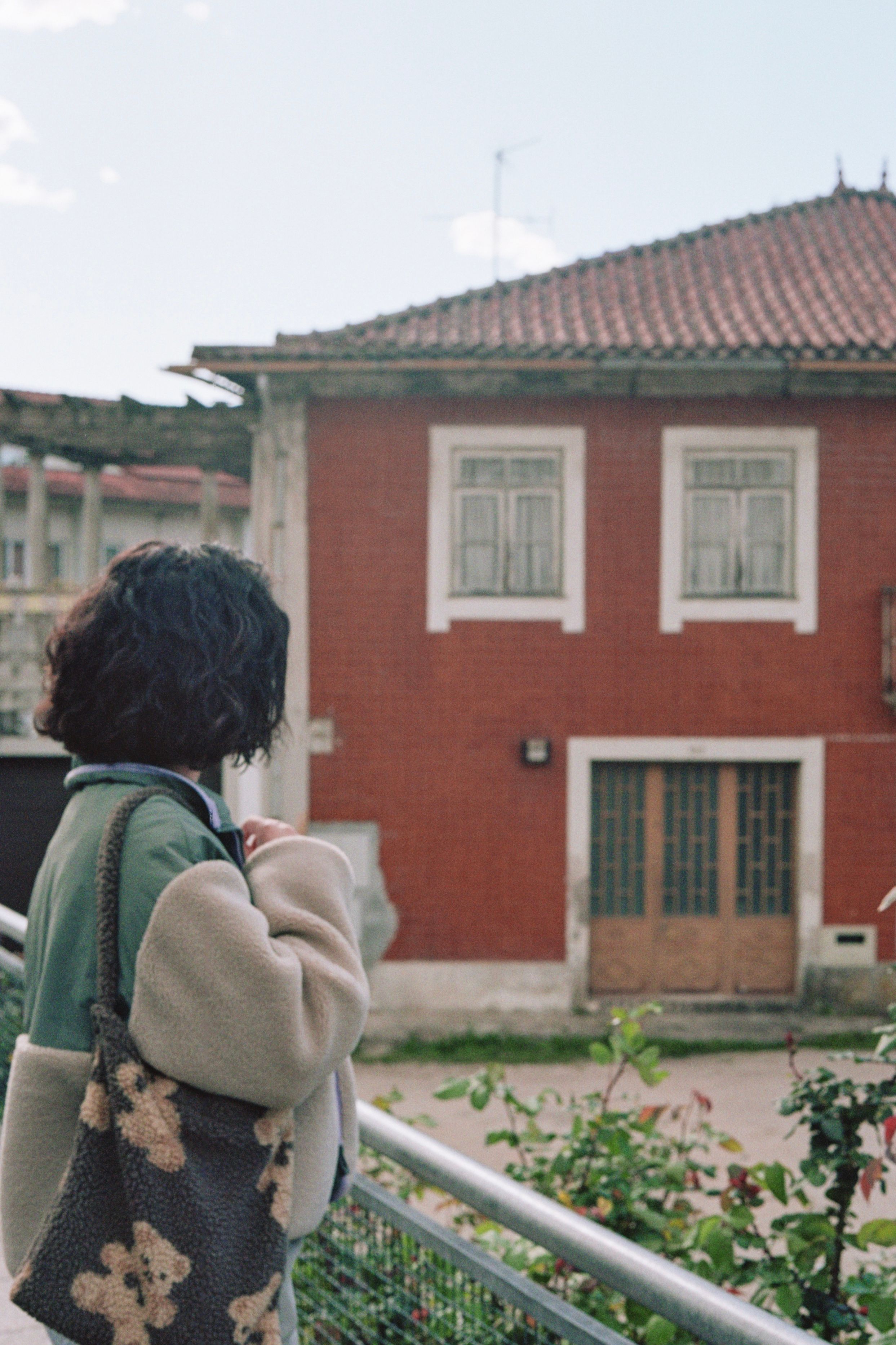A woman with a curly hairstyle stands outside looking at a red brick building.