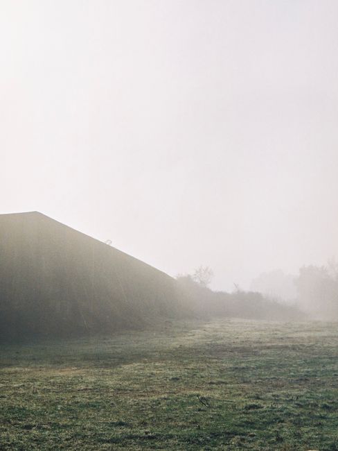 A serene foggy grassland landscape with a distant misty hill, captured in a rural setting during the day.