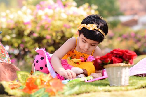 Free A young girl focused on playing with a toy outdoors, surrounded by vibrant flowers. Stock Photo