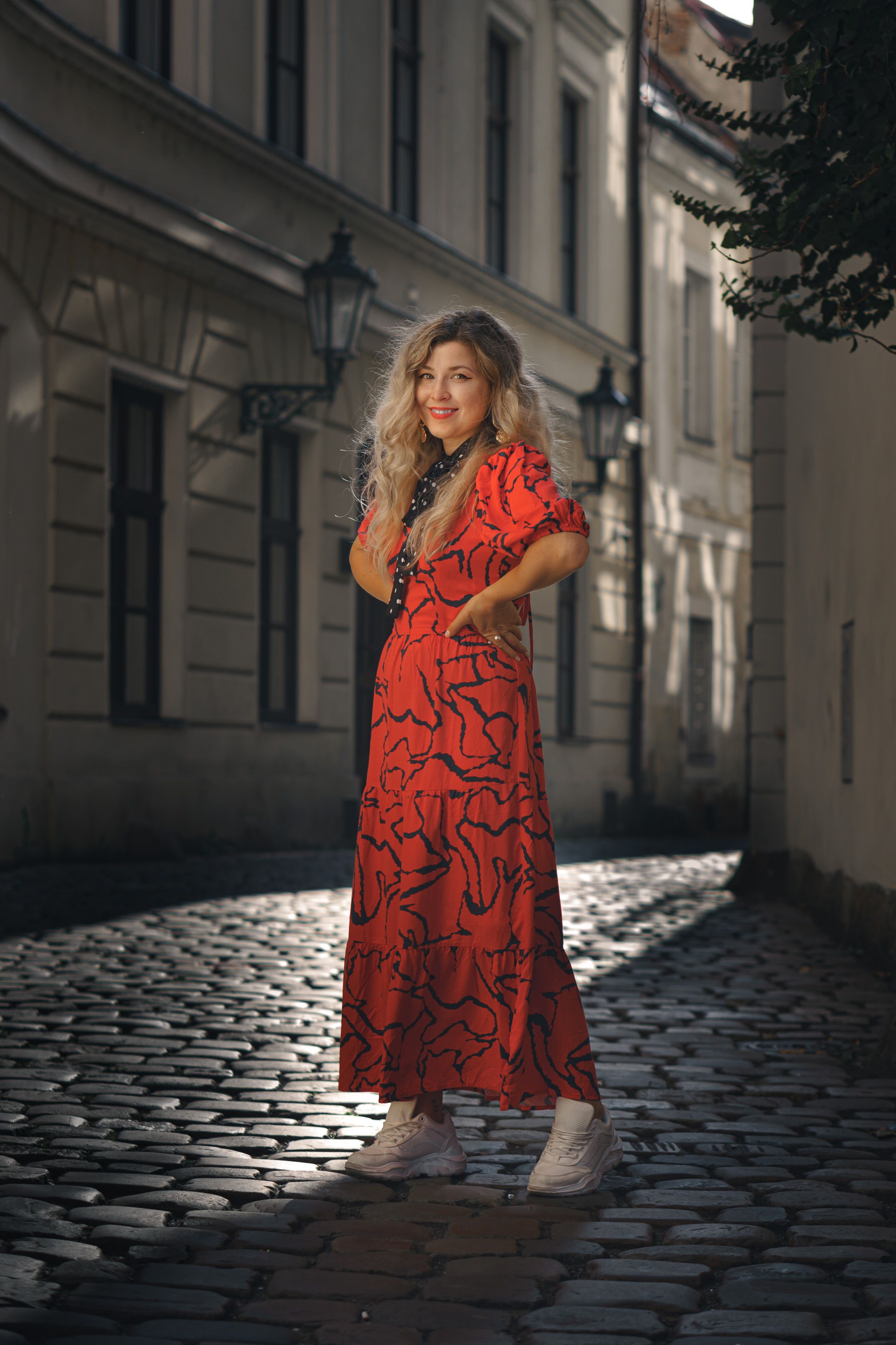 Woman in a vibrant red dress striking a pose on a historic cobblestone street.