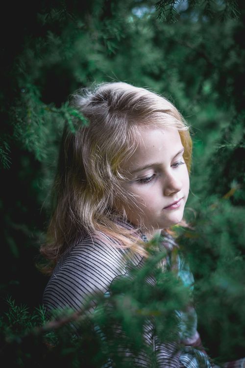 Free A blonde girl stands amidst lush greenery, embodying innocence and tranquility. Stock Photo