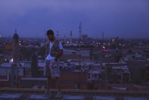 Free A man stands on a rooftop overlooking a cityscape at dusk with dim city lights in the background. Stock Photo