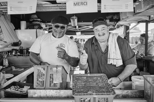Black and white photo of two smiling market vendors giving thumbs up at a food stall.