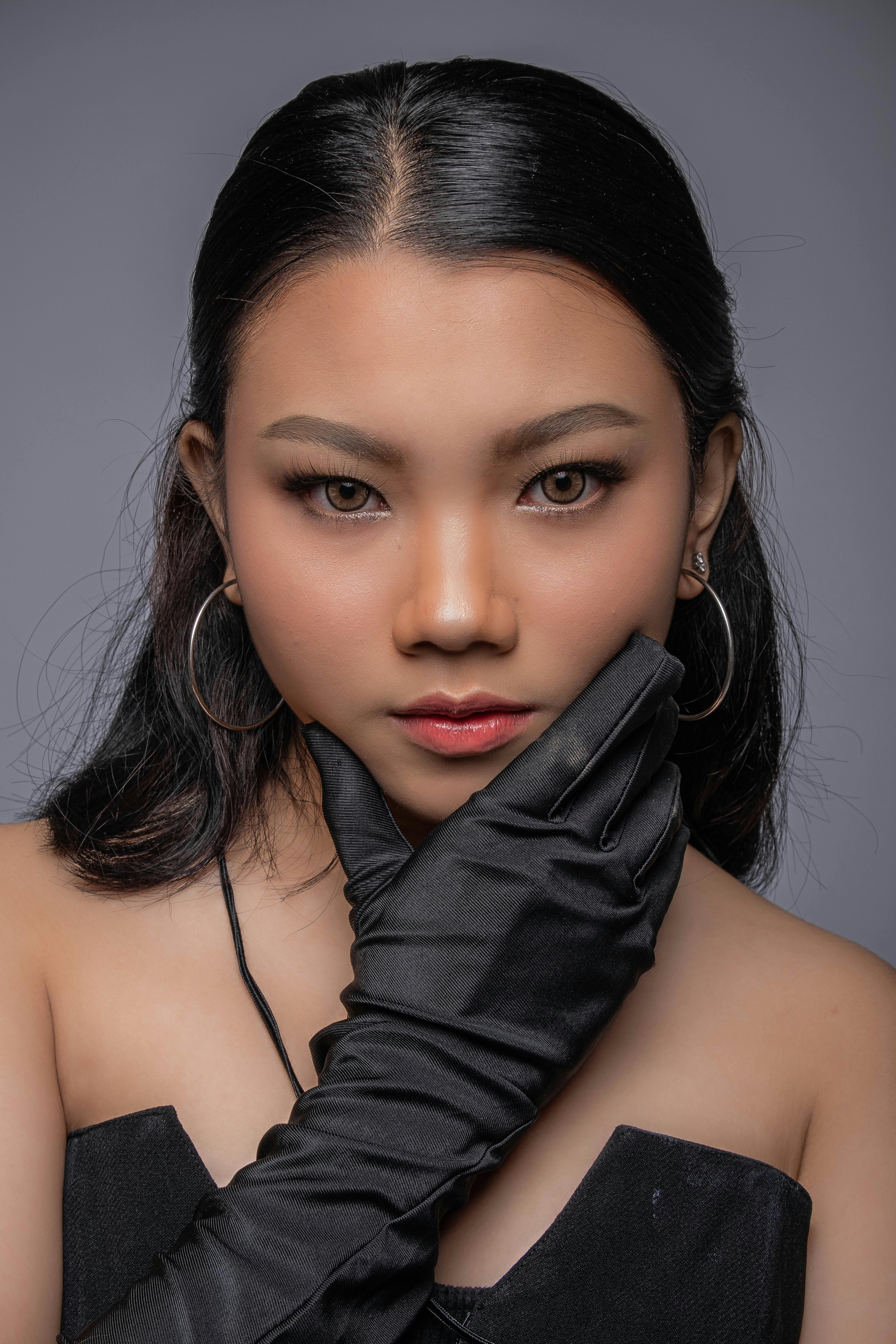 Elegant woman with black gloves and hoop earrings against a gray backdrop, exuding fashion and style.