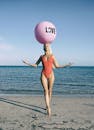在阳光明媚的迈阿密海滩上，一个穿着红色泳衣的女人平衡着一个写着“爱”的粉红色气球