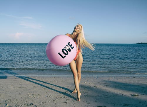 Woman Wearing Orange Swimsuit While Holding Pink Inflatable Beside Body of Water