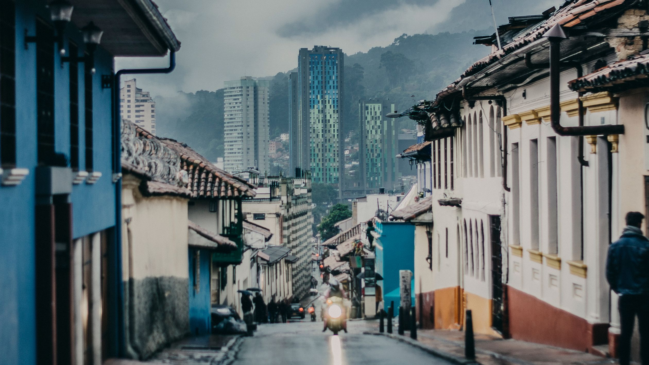 Charming street scene in Bogotá with colorful houses and towering skyscrapers under cloudy skies.