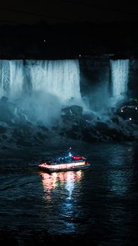 A stunning nighttime view of a tourist boat near illuminated Niagara Falls.