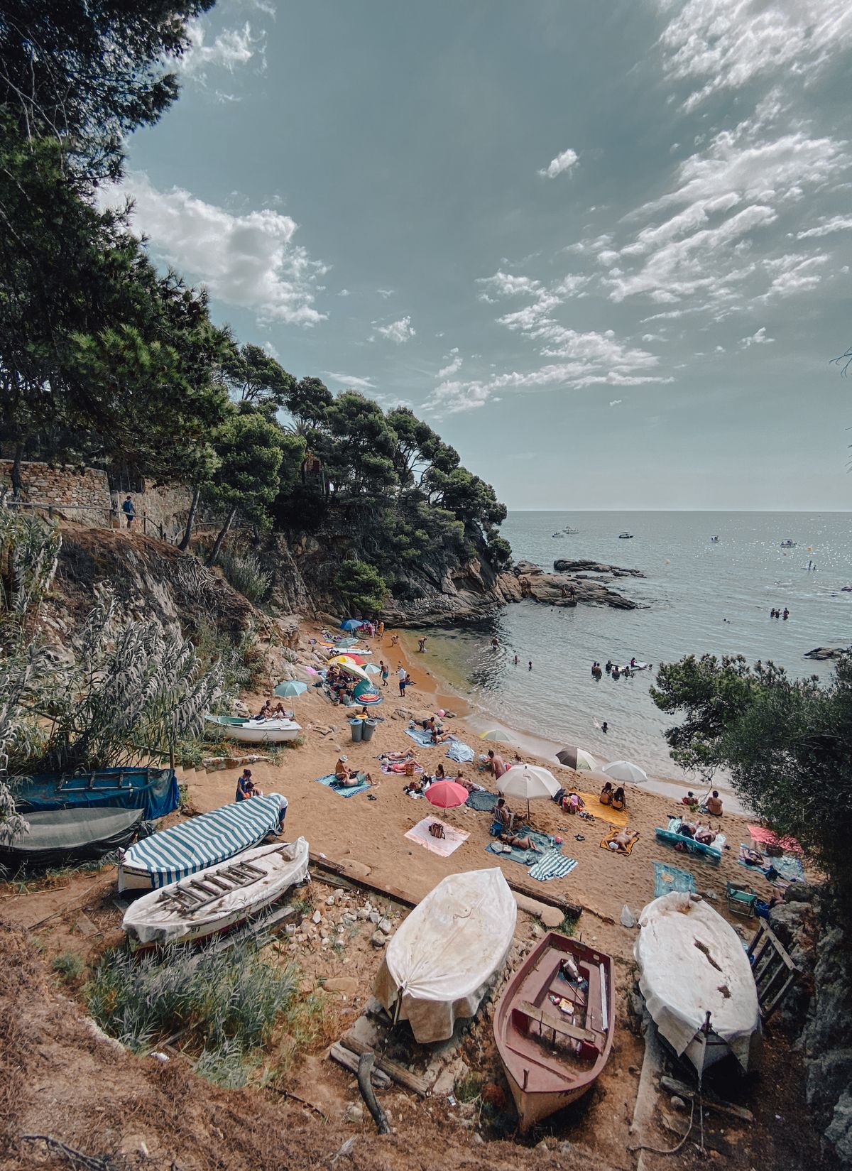 Plaja din Palafrugell cu bărci ancorate și oameni la soare