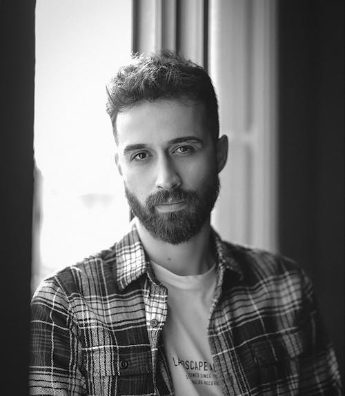 Man in Plaid Shirt Standing Beside a Window