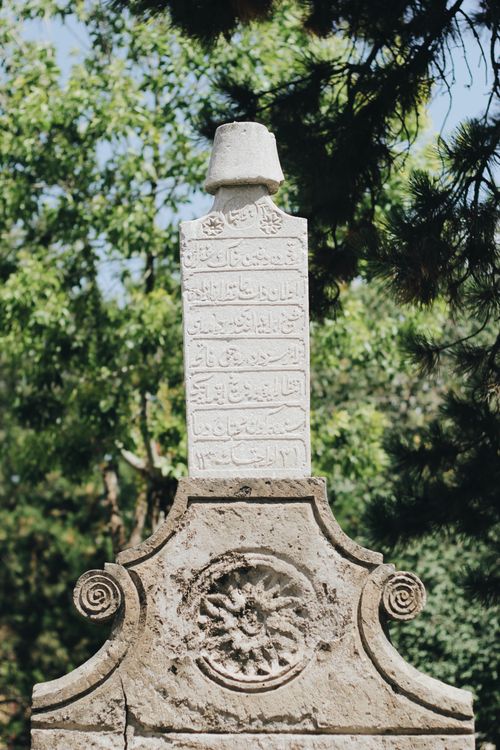 Free An ornate carved tombstone with inscriptions in a lush, green cemetery setting. Stock Photo