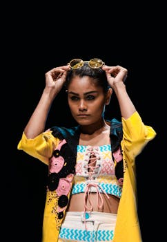 Fashionable woman adjusting sunglasses in vibrant attire on black background.