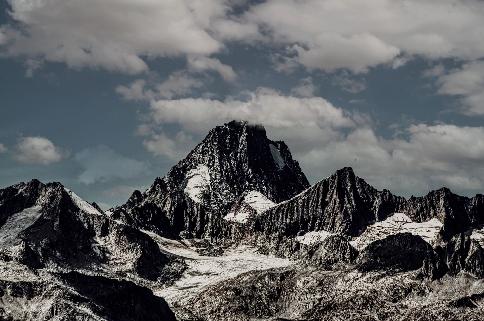 Breathtaking view of snow-capped rugged mountains under a cloudy sky, showcasing nature's raw beauty.