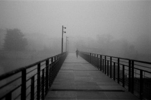 Grayscale Photo of a Person Jogging on a Bridge