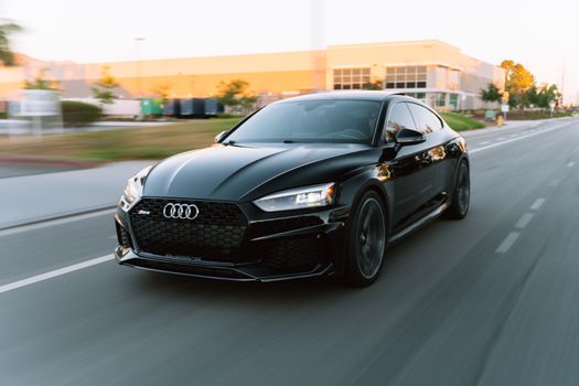 A sleek black Audi RS5 in motion on a city road during daytime.