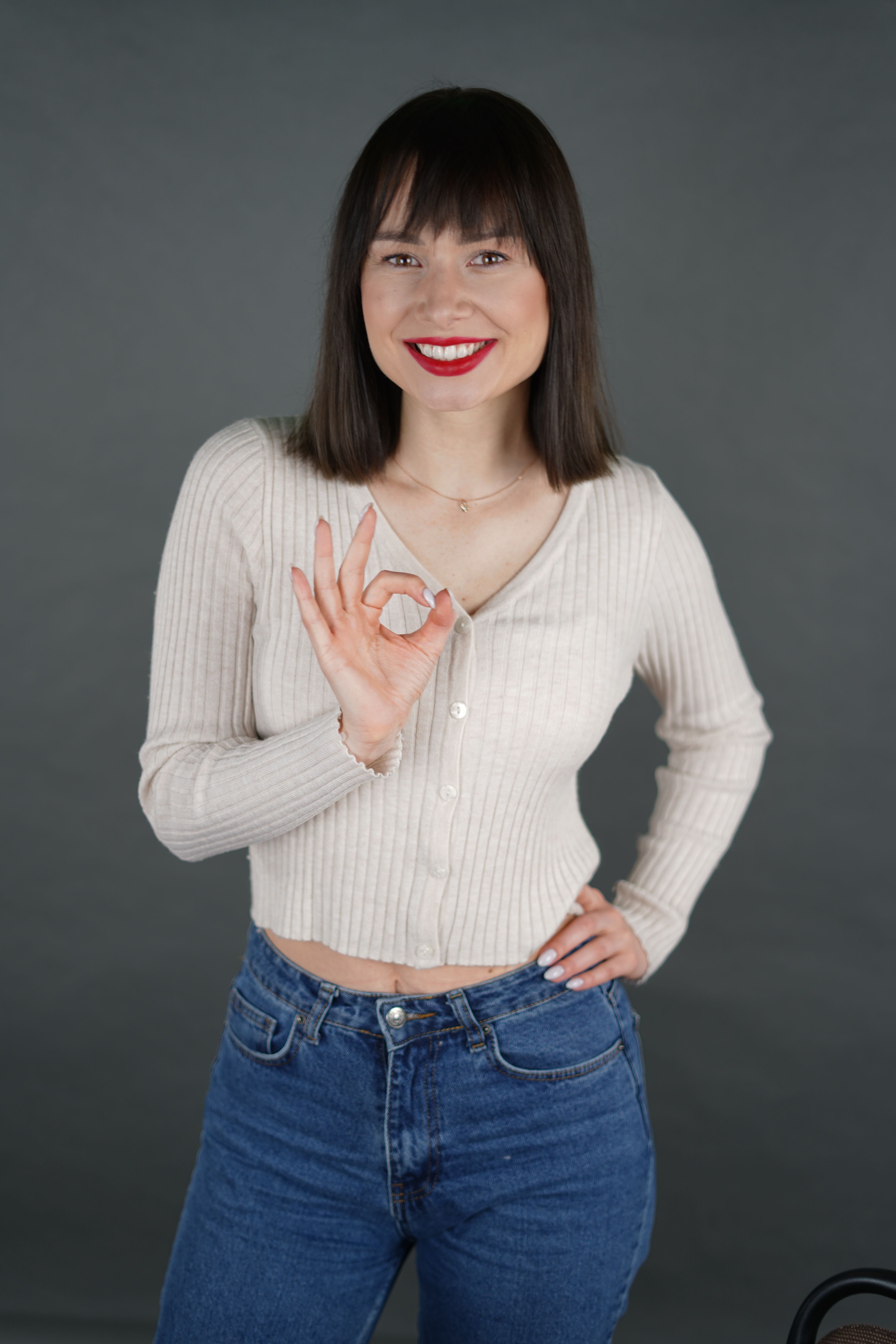 Cheerful woman wearing casual attire giving an OK sign in a studio portrait.