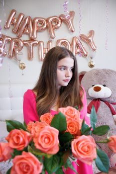 Young woman holding roses with birthday balloons in the background.