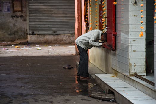 一位老人靠在城市街道的墙上，雨中的他显得格外孤独