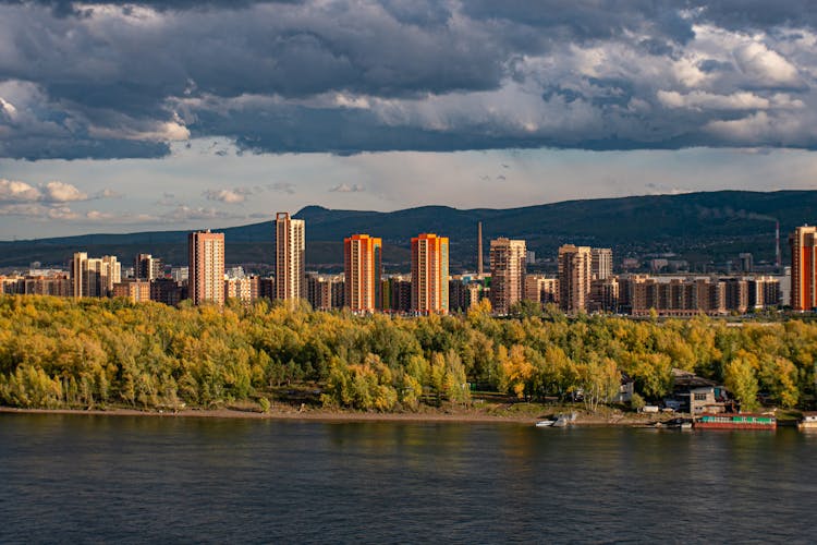 Skyscrapers On River Bank In Mountains Landscape